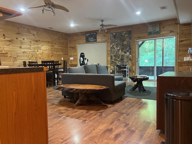 living room with wood-type flooring, a wood stove, ceiling fan, and wood walls