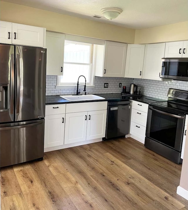 kitchen featuring white cabinetry, sink, stainless steel appliances, tasteful backsplash, and light hardwood / wood-style flooring