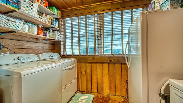 clothes washing area featuring wood walls, washer and dryer, and laundry area