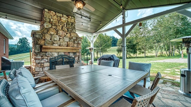 view of patio / terrace with area for grilling, outdoor dining space, an outdoor stone fireplace, and a ceiling fan