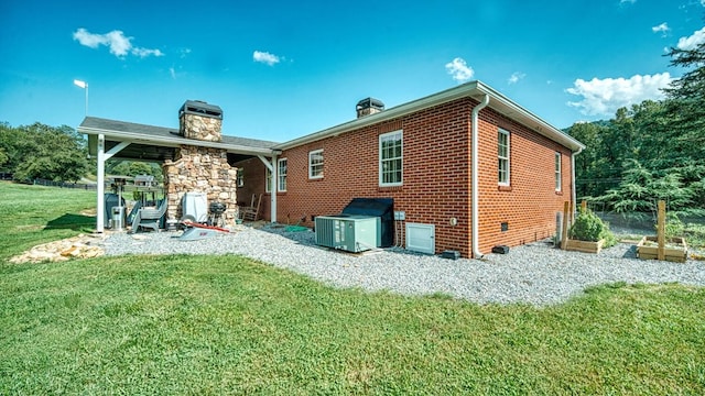 rear view of house featuring a chimney, cooling unit, brick siding, a lawn, and a vegetable garden