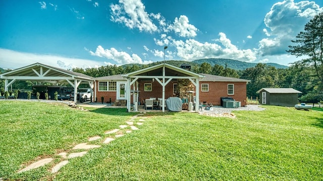 back of house with a lawn, brick siding, a detached carport, and an outbuilding