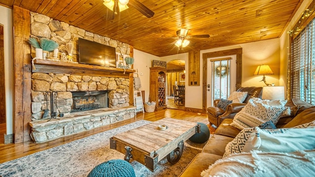 living room with wood finished floors, a ceiling fan, a stone fireplace, arched walkways, and wooden ceiling