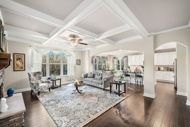 living room with beam ceiling, coffered ceiling, dark wood-style floors, arched walkways, and baseboards