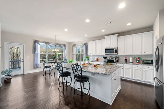 9475 Dunmoore Dr, Cumming, GA 30028 - kitchen with visible vents, light stone countertops, appliances with stainless steel finishes, and dark wood-style flooring