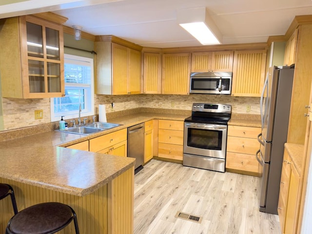 kitchen featuring appliances with stainless steel finishes, tasteful backsplash, light hardwood / wood-style floors, kitchen peninsula, and sink