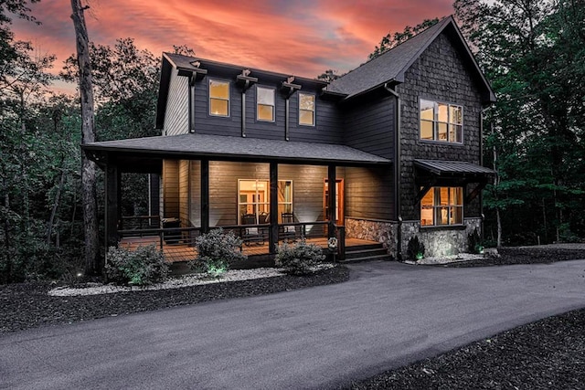 back of property at dusk with covered porch and stone siding