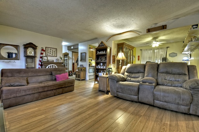 living room featuring a ceiling fan, light wood-type flooring, and a textured ceiling