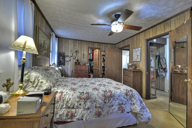 carpeted bedroom featuring wood walls, a textured ceiling, a ceiling fan, and ornamental molding