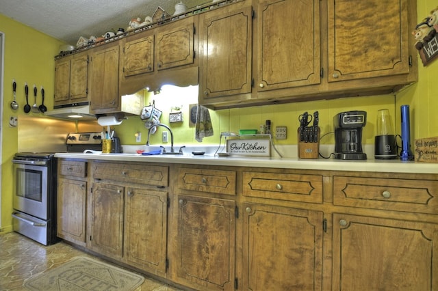 kitchen featuring brown cabinets, under cabinet range hood, stainless steel electric stove, a textured ceiling, and light countertops