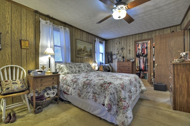 carpeted bedroom featuring wooden walls, ceiling fan, ornamental molding, a closet, and a walk in closet