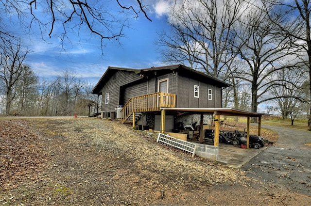 view of property exterior with aphalt driveway, a carport, and stairs