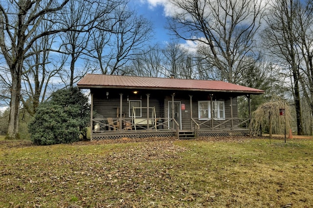 view of front of home featuring a front lawn, a chimney, covered porch, and metal roof