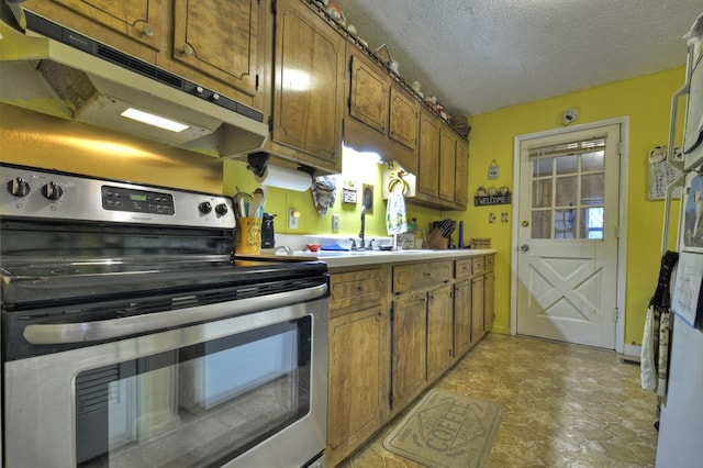 kitchen featuring stainless steel electric range oven, brown cabinetry, a sink, under cabinet range hood, and a textured ceiling