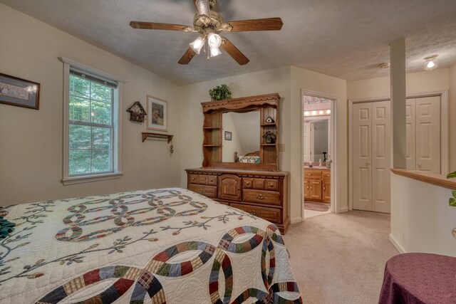 bedroom with ceiling fan, light colored carpet, ensuite bathroom, and a textured ceiling