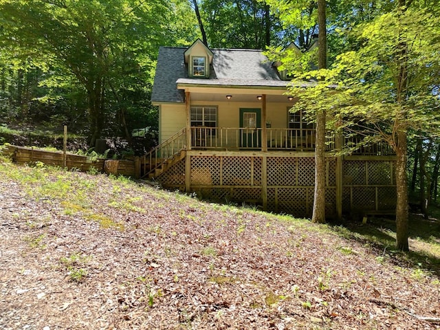 back of house featuring covered porch, a shingled roof, and stairway