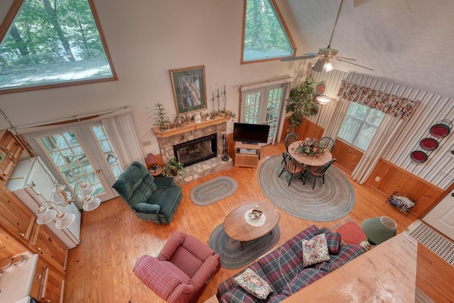 living room with ceiling fan, high vaulted ceiling, hardwood / wood-style floors, and a stone fireplace