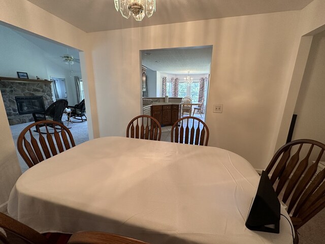 dining space with carpet floors, a stone fireplace, and ceiling fan with notable chandelier