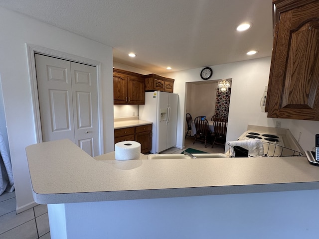 kitchen with stove, dark brown cabinets, kitchen peninsula, light tile patterned flooring, and white fridge with ice dispenser