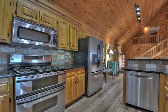 kitchen with wood walls, dark stone counters, light hardwood / wood-style floors, lofted ceiling, and appliances with stainless steel finishes