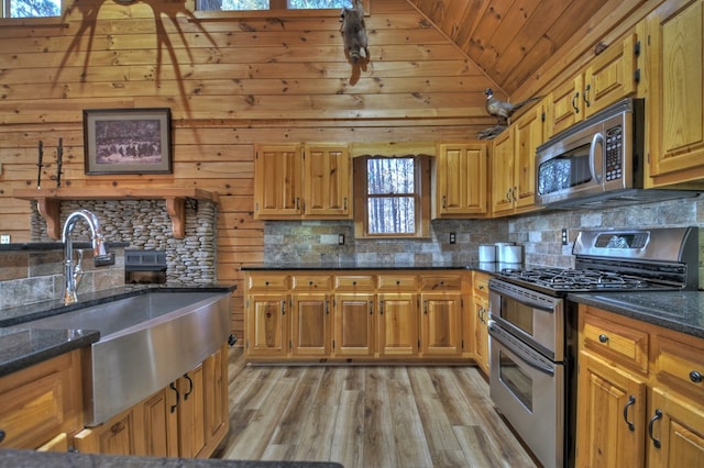 kitchen with appliances with stainless steel finishes, sink, dark stone countertops, and wood walls