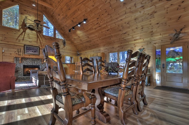 dining space featuring a fireplace, high vaulted ceiling, dark wood-type flooring, and wood walls