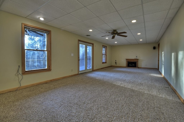 unfurnished living room featuring plenty of natural light, ceiling fan, a drop ceiling, and carpet floors