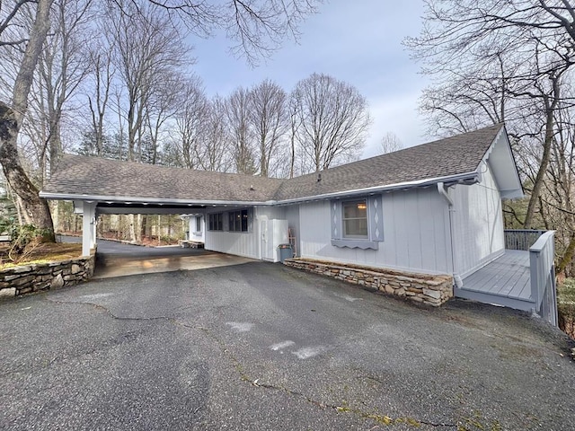 view of front facade featuring an attached carport, driveway, a wooden deck, and roof with shingles