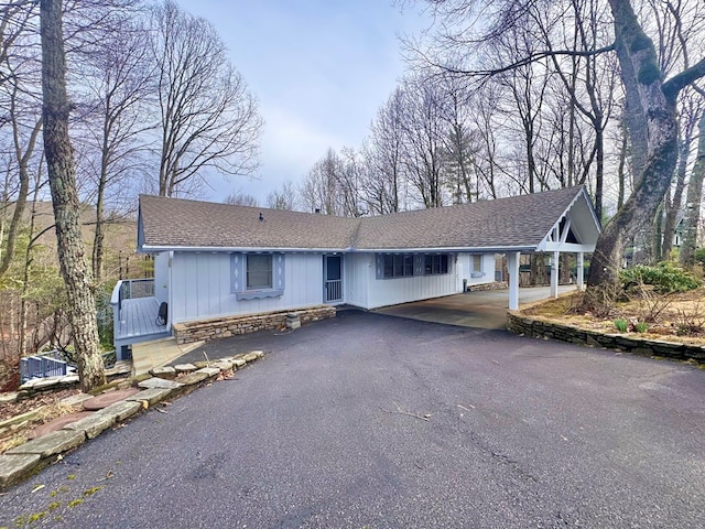 ranch-style home with stone siding, driveway, and roof with shingles