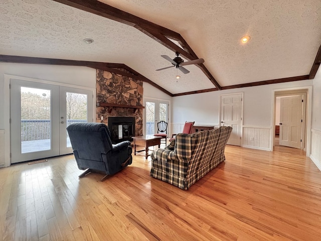 living area with light wood-style floors, lofted ceiling with beams, french doors, and a wainscoted wall