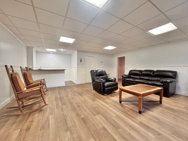 living room featuring light wood-style flooring, a drop ceiling, and wainscoting