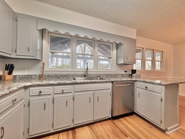 kitchen featuring dishwasher, light wood-type flooring, a peninsula, a textured ceiling, and a sink