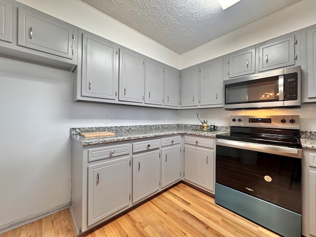 kitchen featuring light countertops, gray cabinets, light wood-style flooring, stainless steel appliances, and a textured ceiling