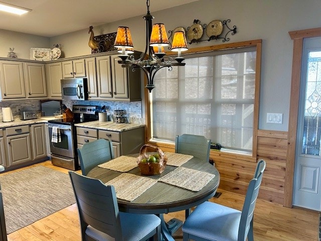 kitchen with gray cabinetry, backsplash, stainless steel appliances, a chandelier, and light wood-type flooring