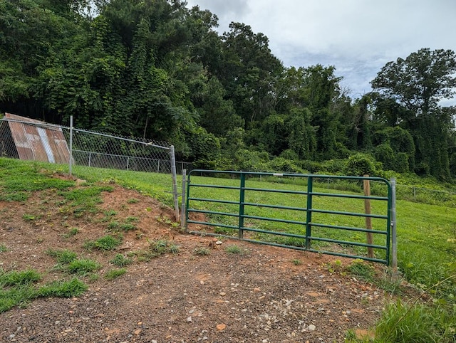 view of gate with a yard, fence, and a wooded view