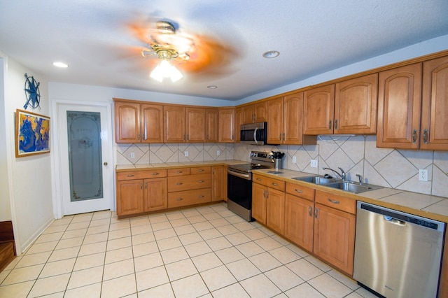 kitchen with brown cabinets, tile countertops, backsplash, appliances with stainless steel finishes, and a sink