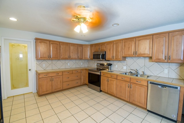 kitchen with light tile patterned floors, brown cabinetry, decorative backsplash, appliances with stainless steel finishes, and a sink