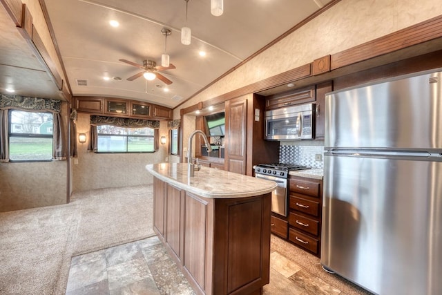 kitchen with light stone counters, stainless steel appliances, vaulted ceiling, ceiling fan, and an island with sink