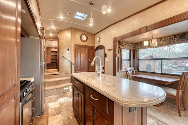 kitchen featuring gas stove, an island with sink, hanging light fixtures, and an inviting chandelier