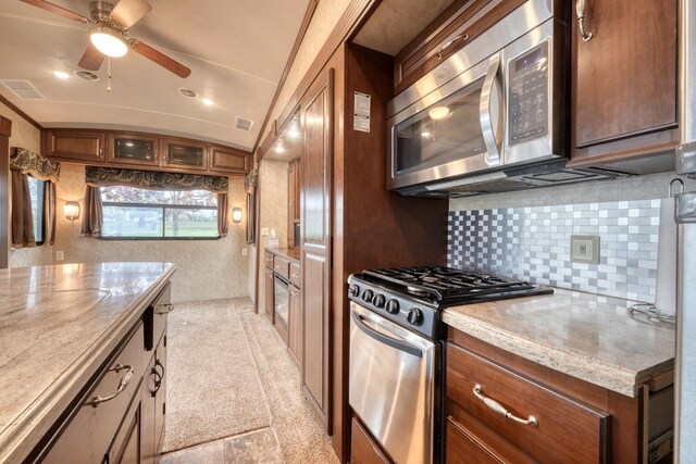 kitchen featuring appliances with stainless steel finishes, tasteful backsplash, light stone counters, vaulted ceiling, and ceiling fan