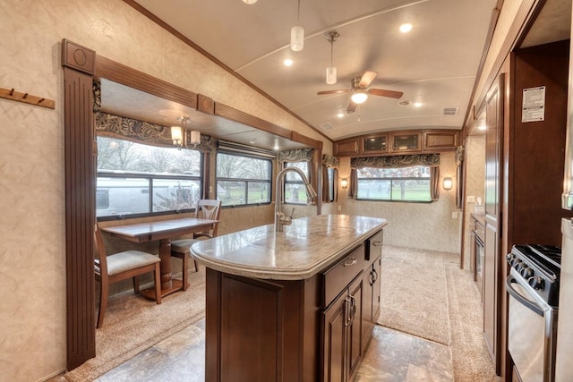 kitchen with stainless steel gas range oven, vaulted ceiling, a kitchen island, ceiling fan with notable chandelier, and ornamental molding