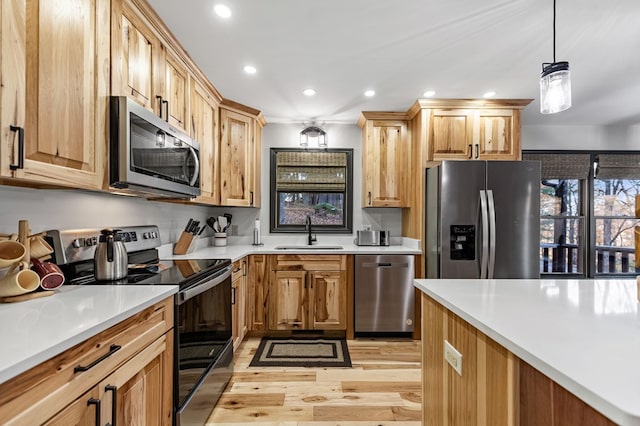 kitchen featuring appliances with stainless steel finishes, decorative light fixtures, sink, and light hardwood / wood-style flooring