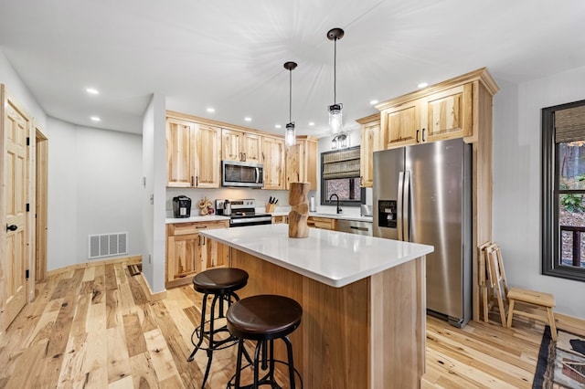 kitchen featuring stainless steel appliances, decorative light fixtures, light brown cabinetry, and a kitchen island