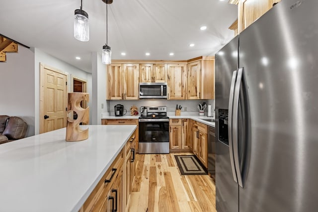 kitchen with light brown cabinets, stainless steel appliances, hanging light fixtures, and light wood-type flooring