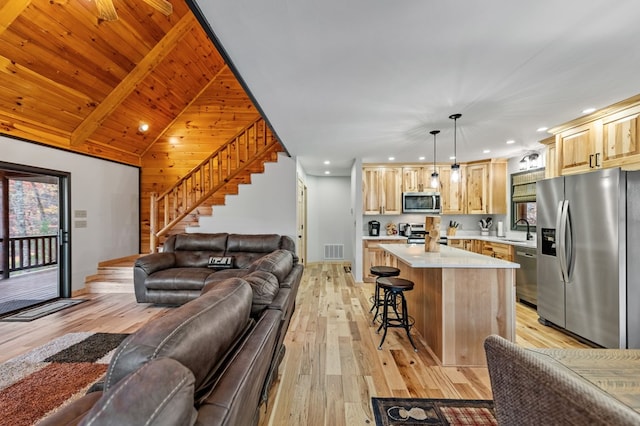 kitchen featuring sink, stainless steel appliances, a center island, light brown cabinetry, and decorative light fixtures