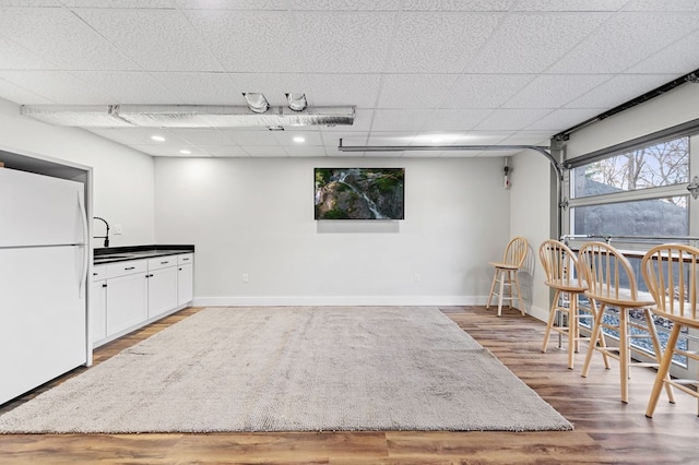 interior space featuring white refrigerator, wood-type flooring, a drop ceiling, and white cabinets