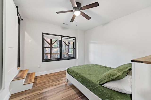 bedroom featuring ceiling fan, wood-type flooring, and a barn door