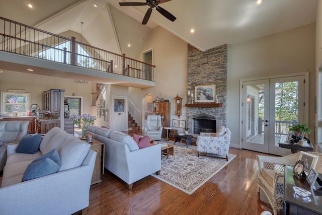 living room featuring hardwood / wood-style floors, high vaulted ceiling, french doors, ceiling fan, and a fireplace