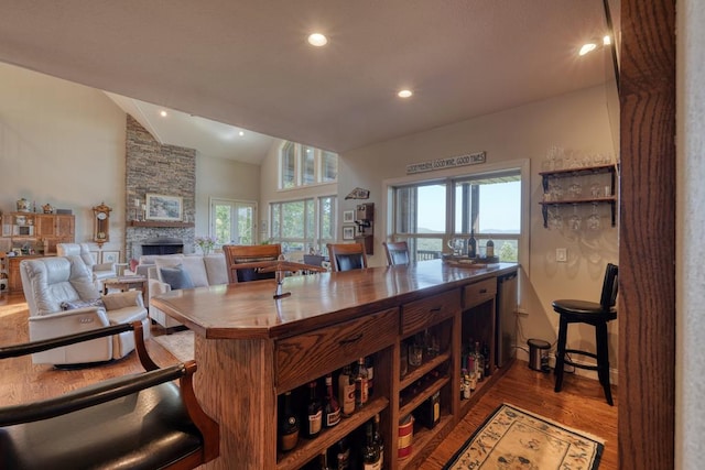 kitchen with hardwood / wood-style flooring, dishwasher, a stone fireplace, and vaulted ceiling