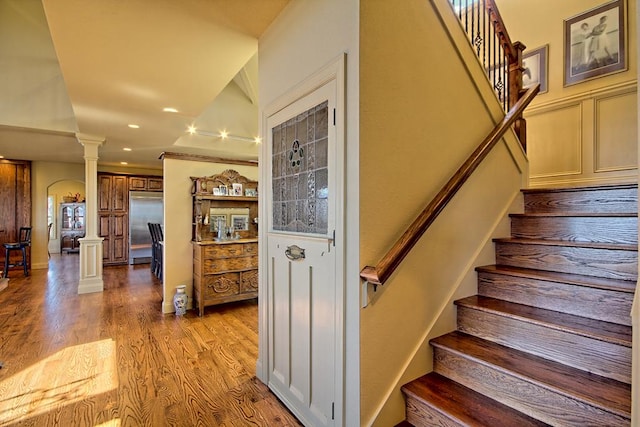 staircase featuring hardwood / wood-style floors, ornate columns, and crown molding